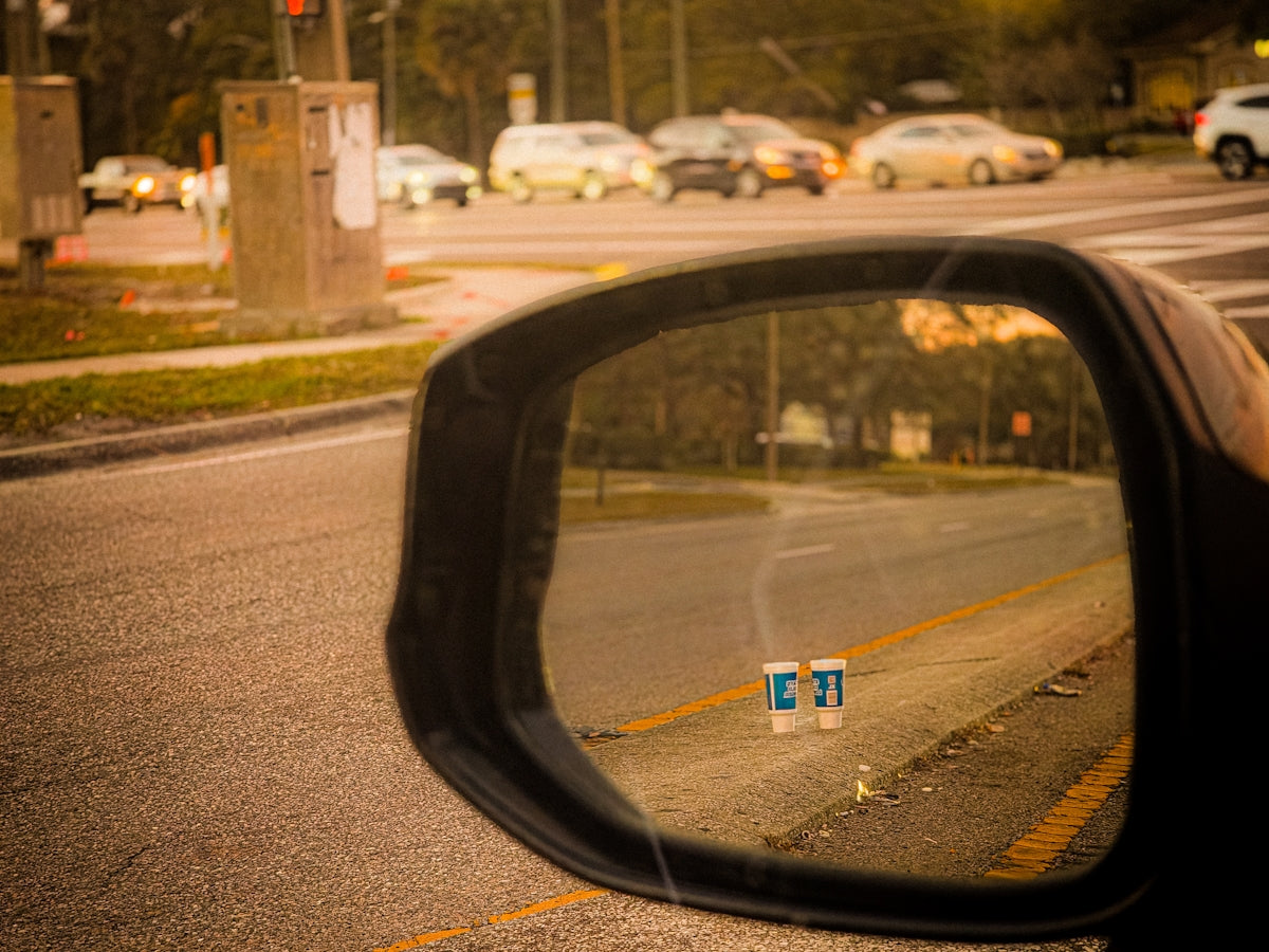 Two disposable coffee cups on the roadside seen in mirror.